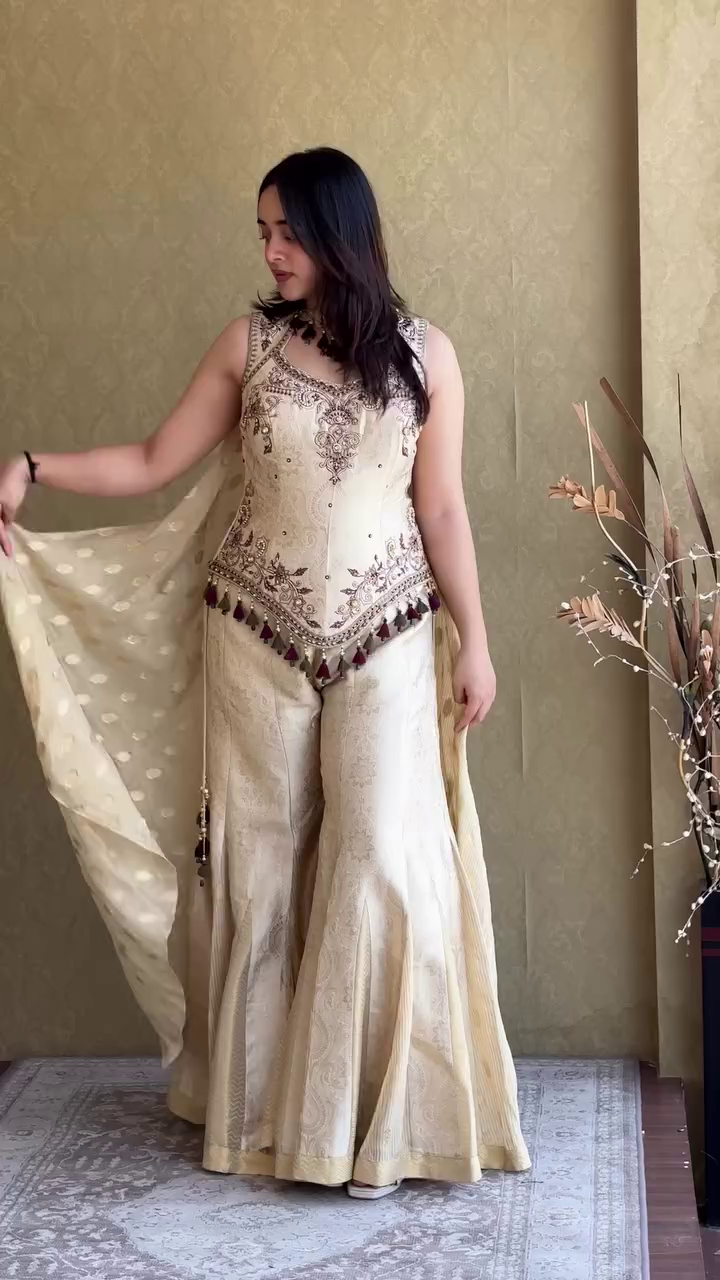Elegant Ivory Cream Embroidered Sharara Style Palazzo Suit with Designer Sleeveless Peplum Top, Traditional Tassel Detailing, and Matching Dupatta for Weddings, Festivals, and Special Occasions