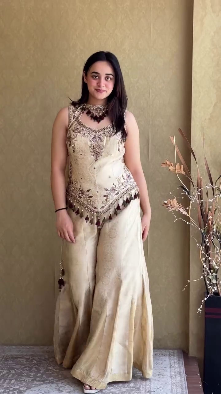 Elegant Ivory Cream Embroidered Sharara Style Palazzo Suit with Designer Sleeveless Peplum Top, Traditional Tassel Detailing, and Matching Dupatta for Weddings, Festivals, and Special Occasions