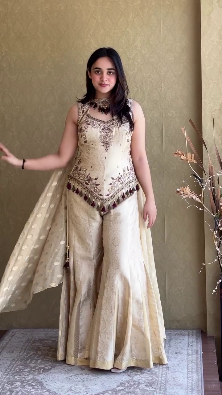 Elegant Ivory Cream Embroidered Sharara Style Palazzo Suit with Designer Sleeveless Peplum Top, Traditional Tassel Detailing, and Matching Dupatta for Weddings, Festivals, and Special Occasions